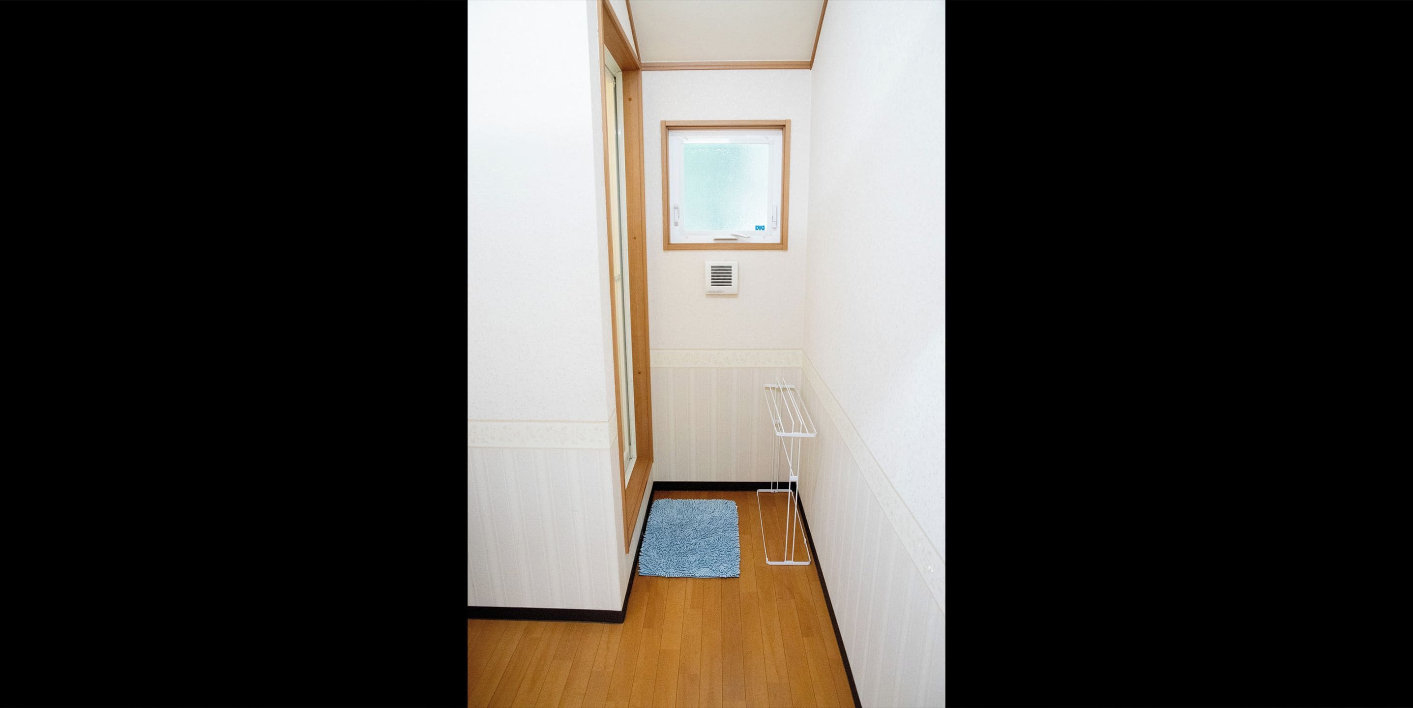 A narrow hallway with wooden flooring, a blue rug, a window with blinds, and a white radiator.