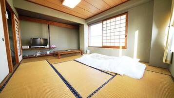 A traditional Japanese room with tatami flooring, a futon bed, a television, and a sliding door.