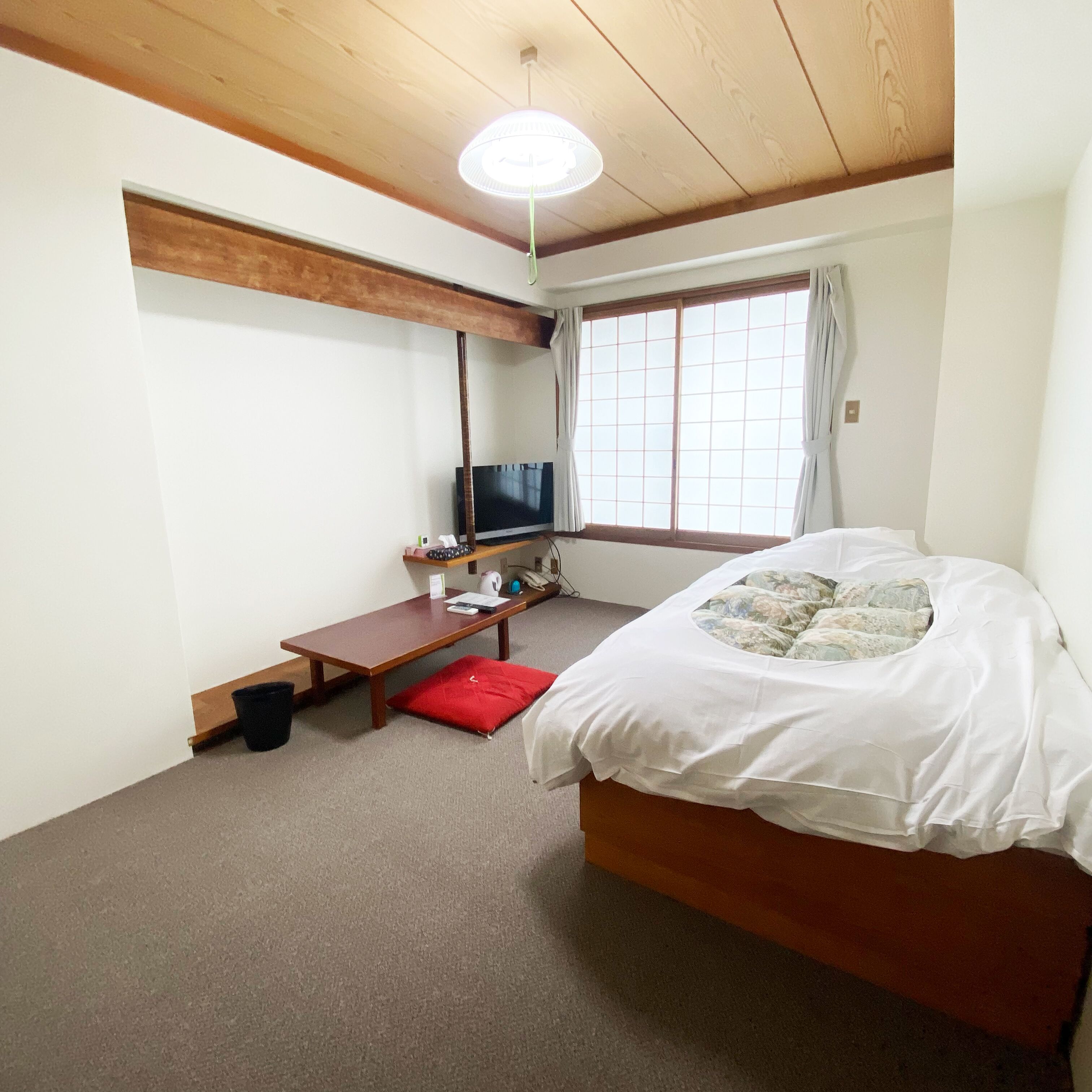 Une chambre à coucher avec un lit, un bureau, une télévision et une fenêtre avec des rideaux.