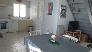 A compact kitchen with a stove, sink, and white cabinets. There is a dining table with a vase of flowers.