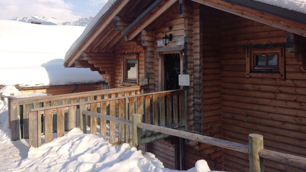 Une cabane en bois avec un toit enneigé et une véranda en bois.