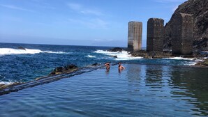 A coastal scene with clear water, rocky cliffs, and two tall stone structures. - REST ENJOYING THE VIEWS OF THE SEA AND THE MOUNTAIN (HERMIGUA)