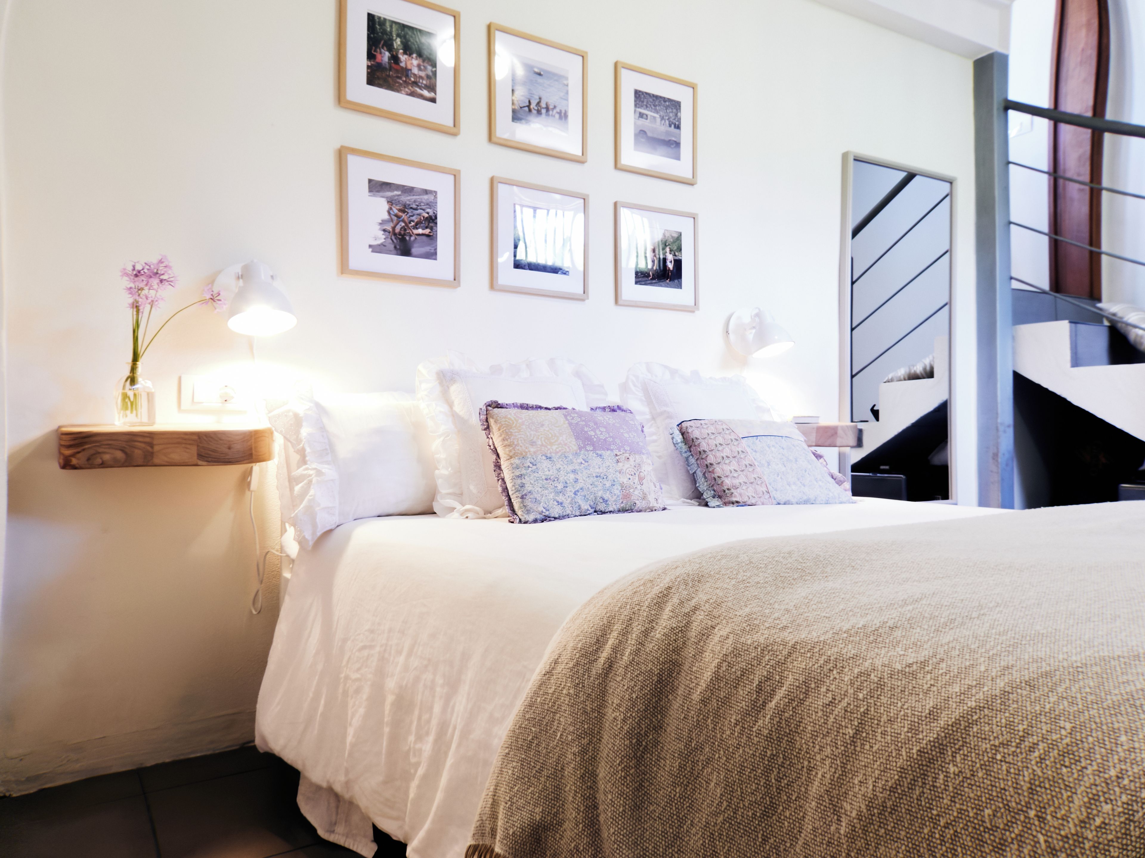 Una camera da letto con un letto, cuscini, un comodino con una lampada e quadri appesi al muro.