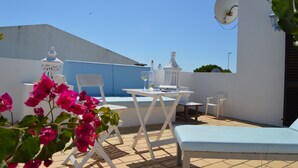 En tagterrasse med hvidt bord, stole, en lille sofa og en parabol.