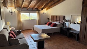 A bedroom with a bed, a sofa, a table, and a desk. There are windows and curtains.