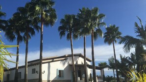 A white building with a tiled roof, surrounded by palm trees and a well-maintained lawn.