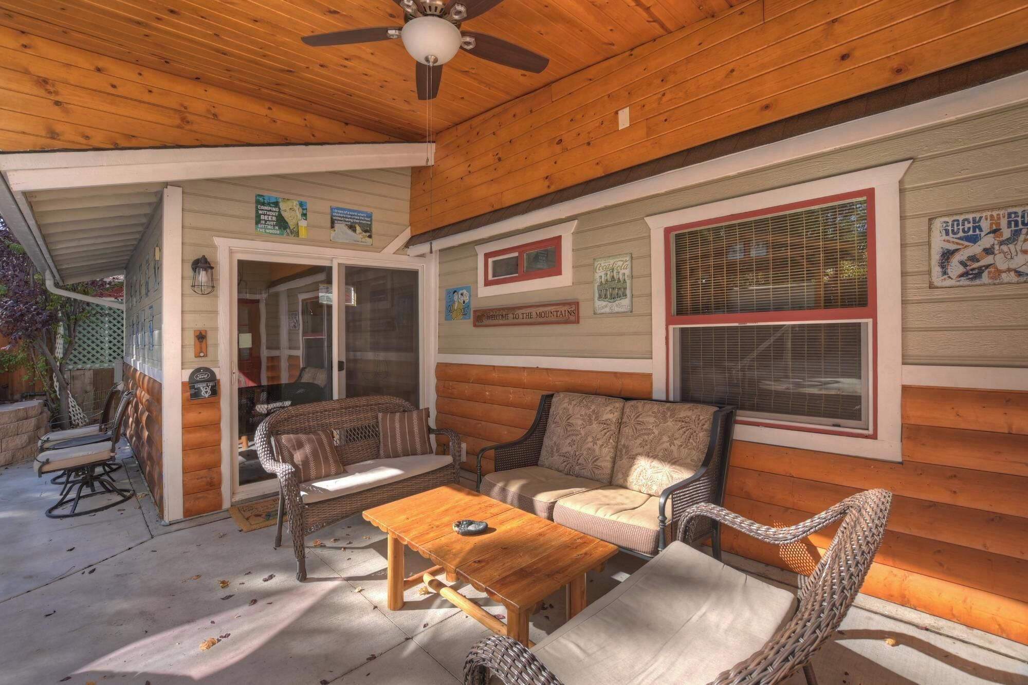 A covered patio area with wicker furniture, a wooden table, and a ceiling fan.