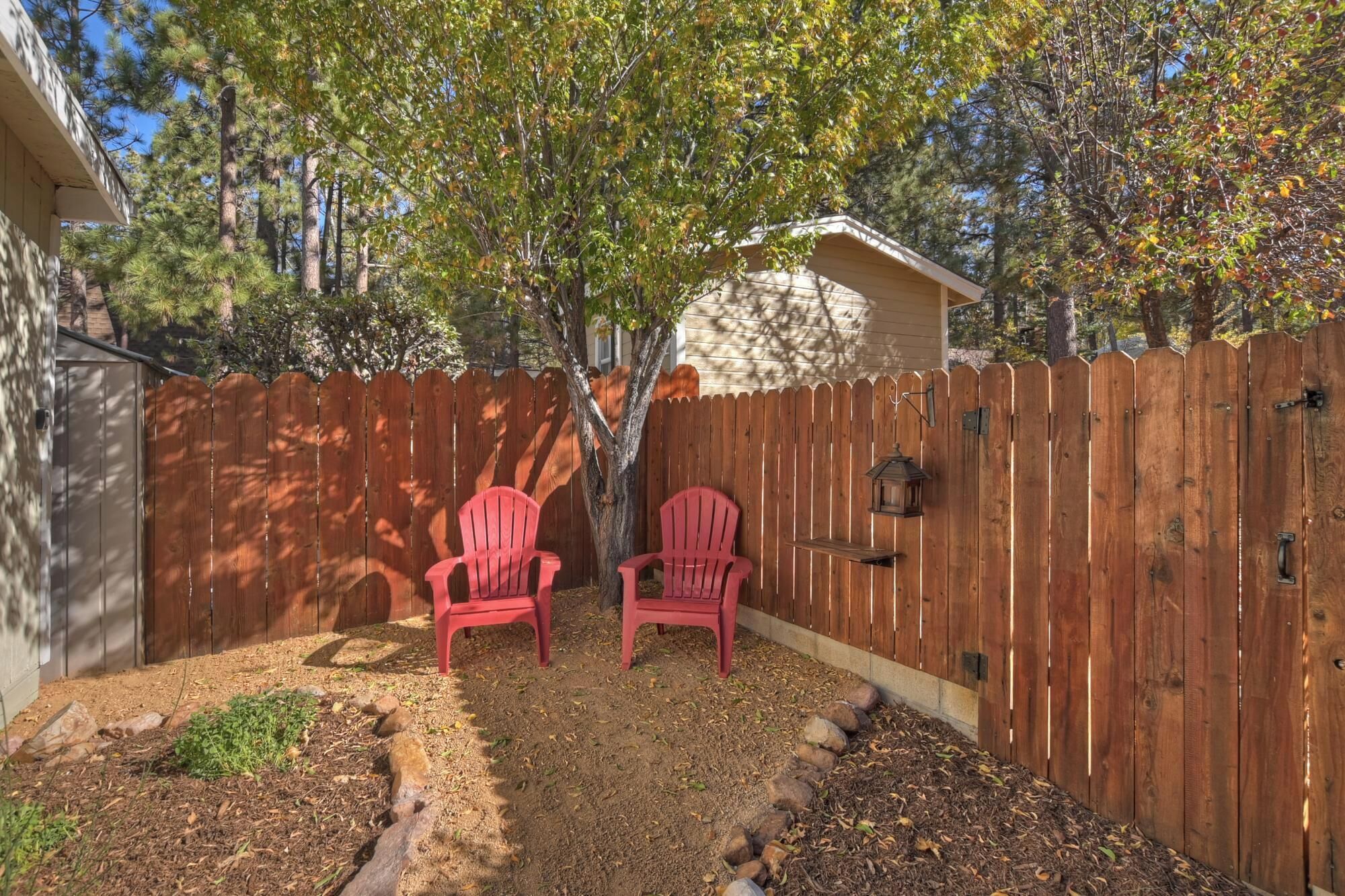 Ein Garten mit Holzparkanlage, zwei roten Adirondack-Stühlen und einem Baum.