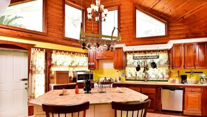 A kitchen with wooden cabinets, a central island with chairs, a chandelier, and a view of the outdoors through large windows. - Villa Gina Beachfront Villa  (Cap estate)