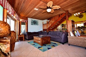 A spacious living room with a wooden ceiling, a large sofa, a coffee table, and a staircase leading to another level.