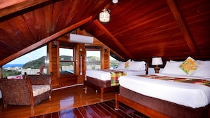 A wooden attic bedroom with a bed, a chair, and a view of the city. - Villa Gina Beachfront Villa  (Cap estate)