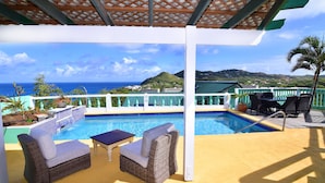 A covered outdoor pool area with wicker furniture and a view of the ocean. - Villa Gina Beachfront Villa  (Cap estate)