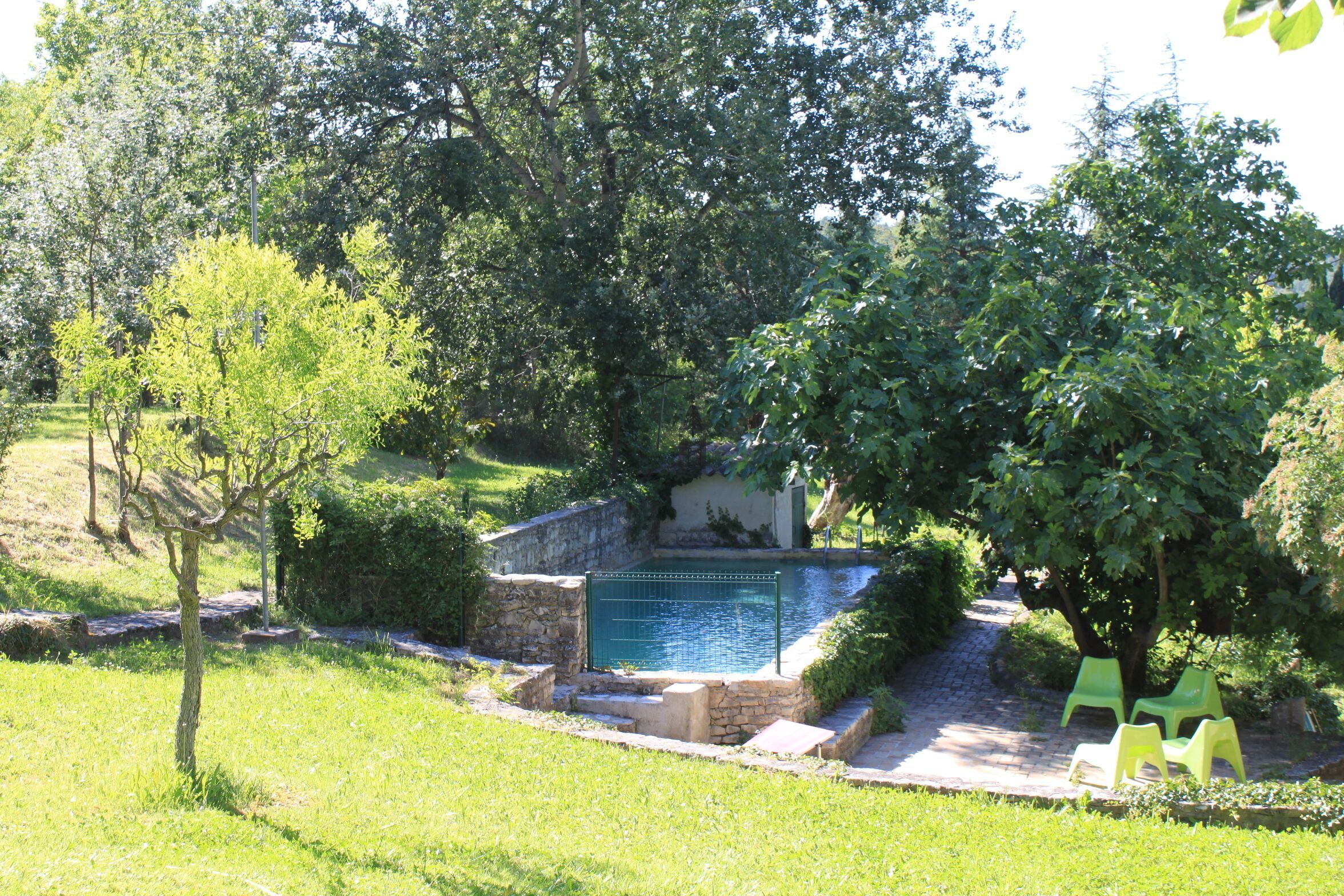 Una piscina rodeada de muros de piedra y follaje, con dos sillas verdes cerca.