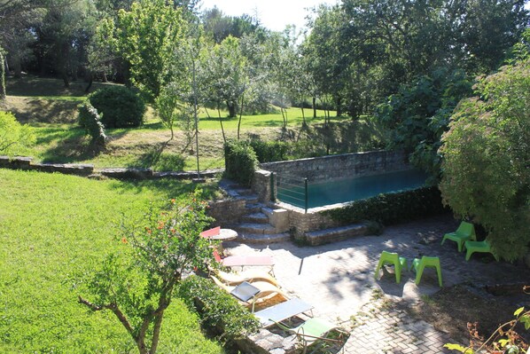 Un patio con piscina, escalones de piedra y sillas verdes.