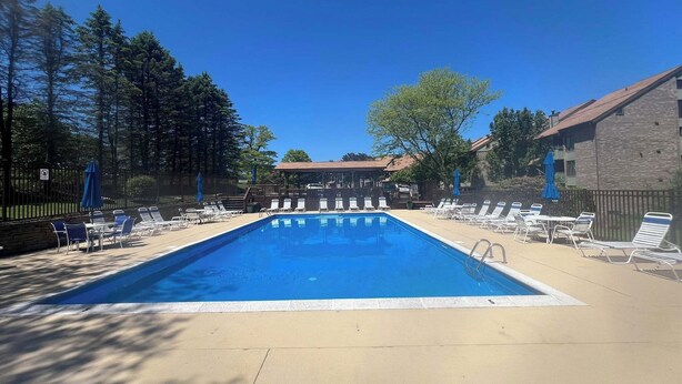 A rectangular swimming pool with lounge chairs and umbrellas, surrounded by a fence and trees. - Spectacular Seven Springs Skiing and golfing in Pennsylvania (Champion)
