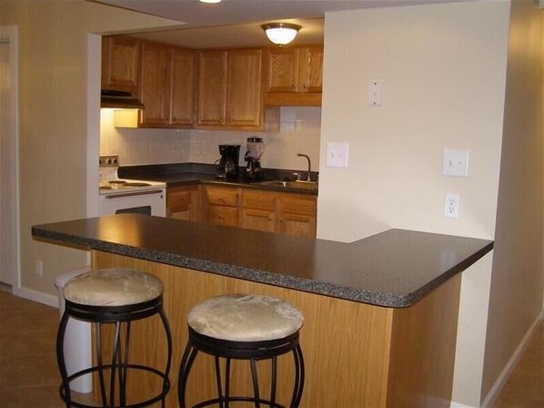 A kitchen with wooden cabinets, a granite countertop, and two stools.