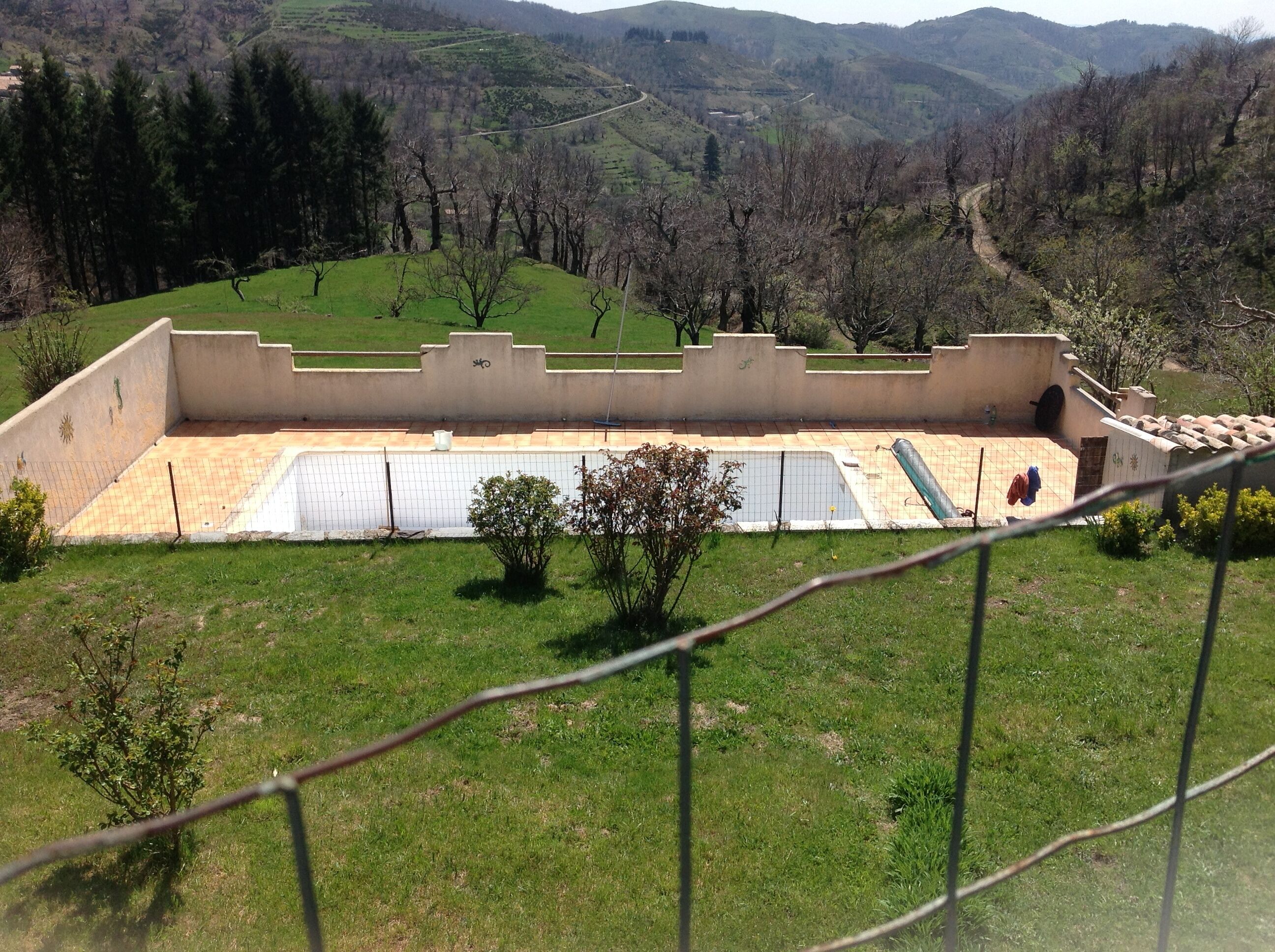 A view of a swimming pool with a tiled deck and a fence.
