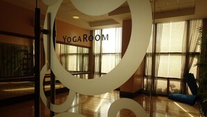 Une salle de yoga avec une grande enseigne, un plancher en bois et de grandes fenêtres ornées de rideaux légers.