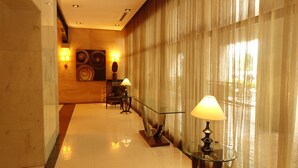 Un couloir d’hôtel avec une table en verre, une lampe et un mur orné d’œuvres d’art.