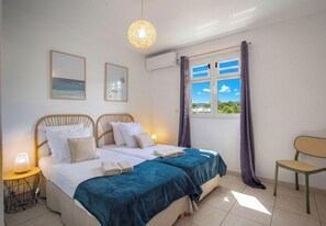 Un lit double avec deux oreillers, une table de chevet avec une lampe, une fenêtre avec des rideaux et une chaise.