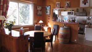 Une cuisine aux murs lambrés, avec un coin repas, des meubles de rangement en bois et une grande fenêtre.