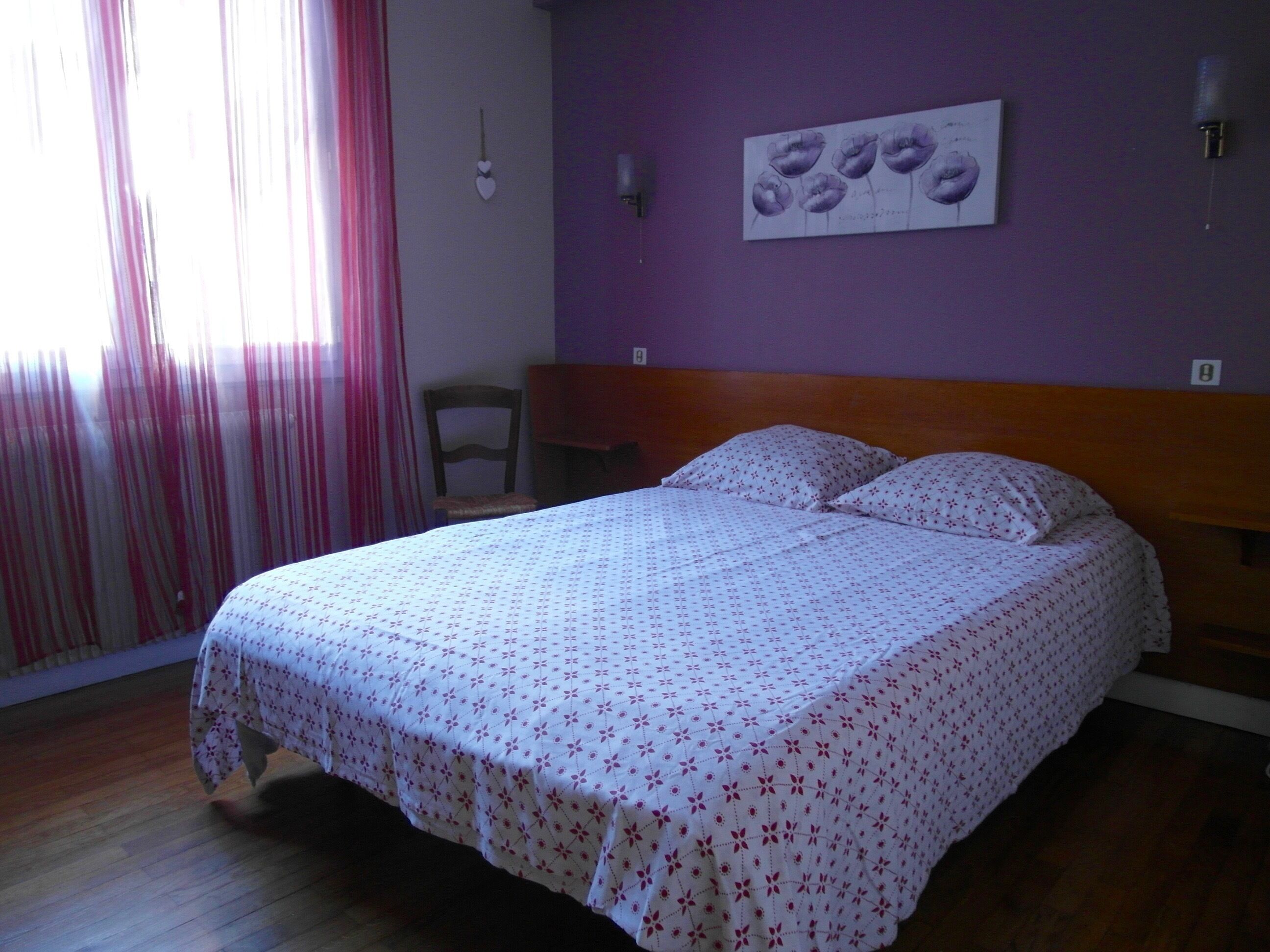 Una camera da letto con un letto, una sedia, un muro decorato con un dipinto floreale e una finestra con tende.