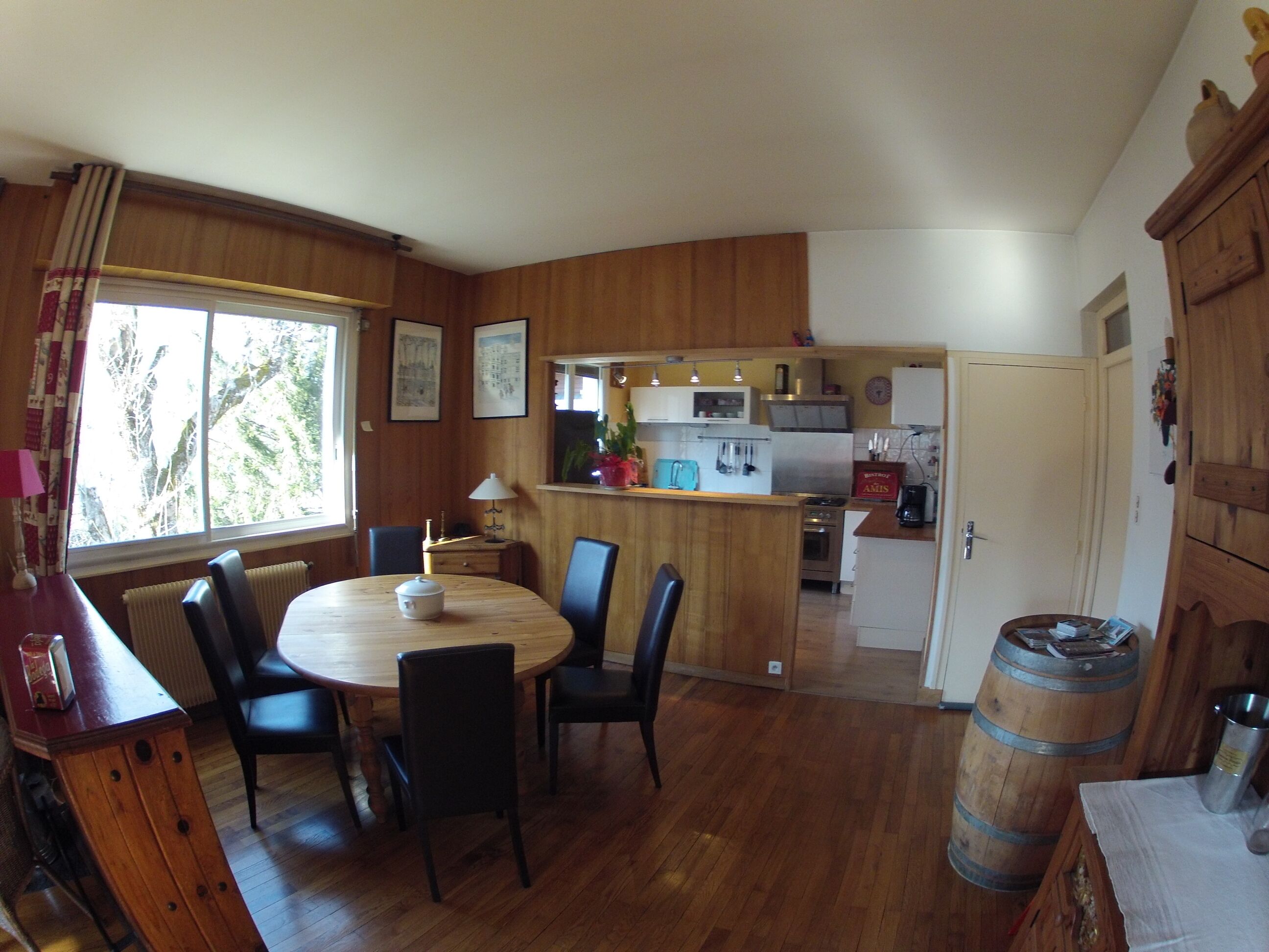 Una cocina compacta con armarios de madera, una mesa de comedor con sillas y un ventanal con cortinas.