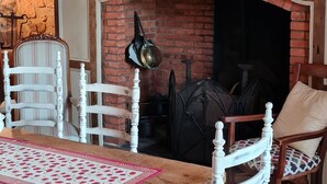 Ein Essbereich mit Kamin aus Ziegelsteinen, weißen Stühlen und einem Tisch mit gemustertem Läufer.