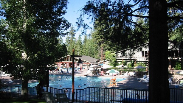 A pool area with lounge chairs and umbrellas, surrounded by trees and a building with a roof. - IMMACULATE 3BR SKI TOWNHOME INSIDE NORTHSTAR RESORT! (Truckee)