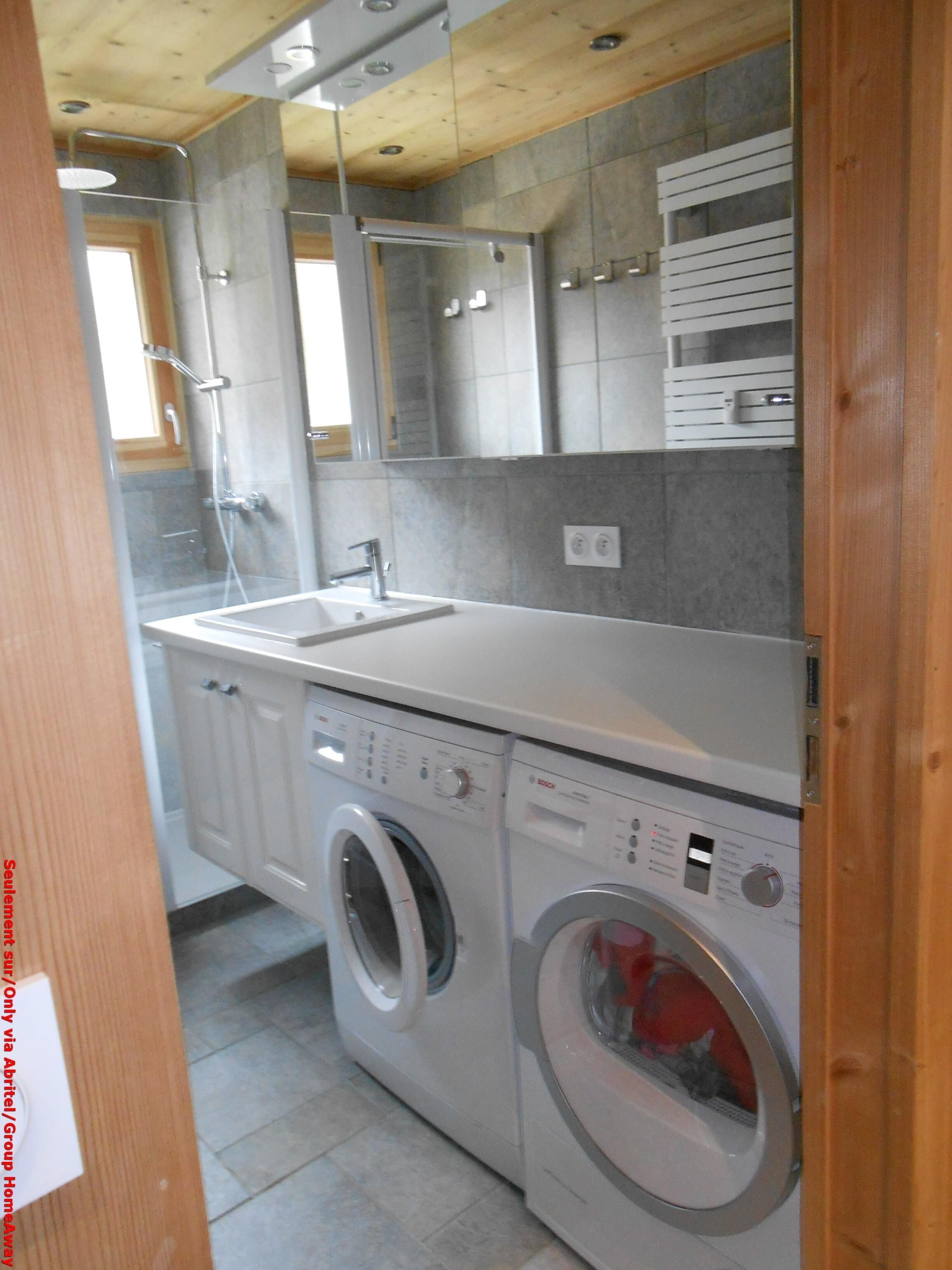 A compact laundry room with a washing machine, a sink, and a shower.