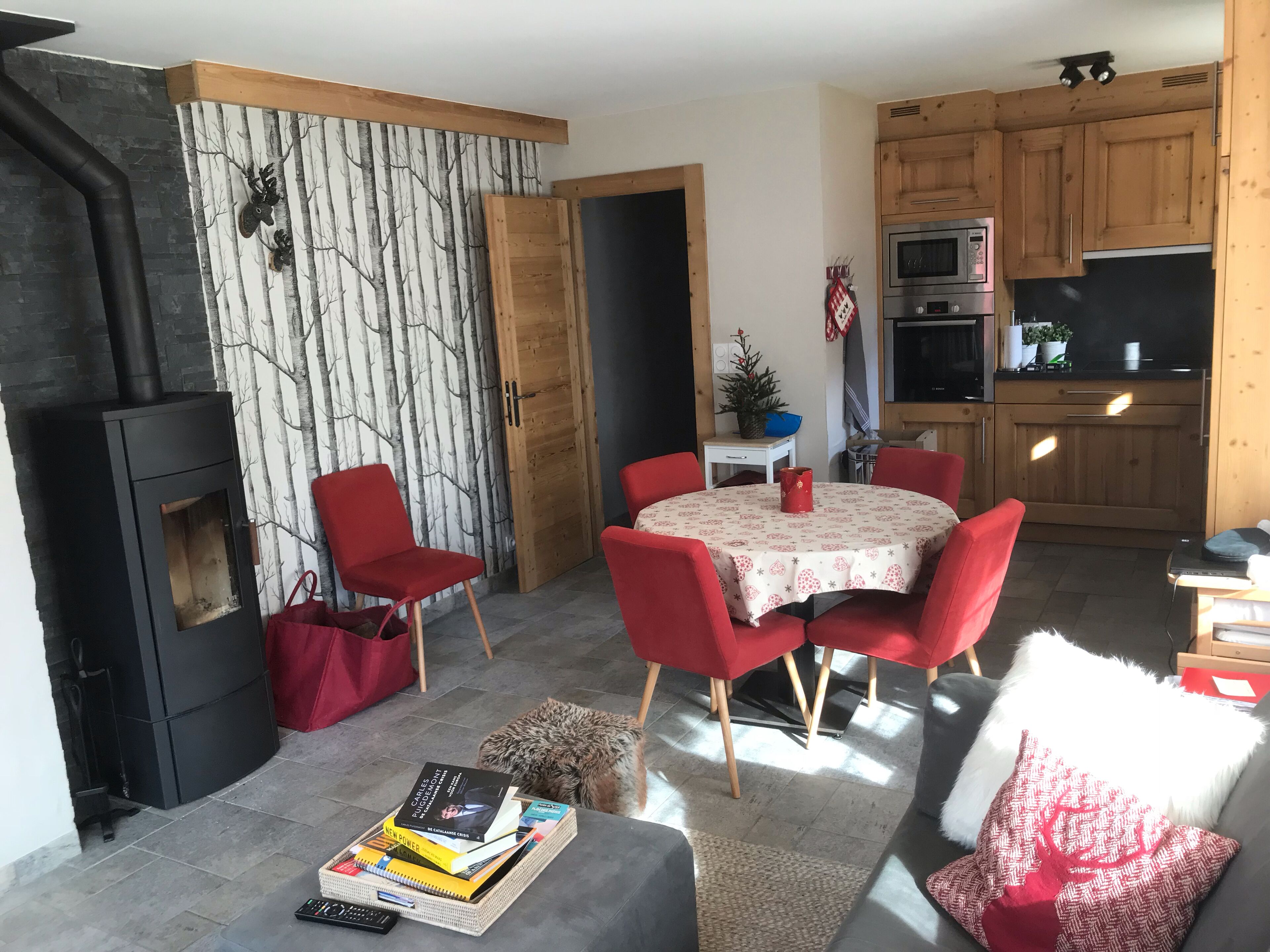 Un salon chaleureux avec une cheminée, un coin repas avec des chaises rouges et une cuisine avec des meubles en bois.