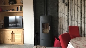 A living room with a black wood-burning stove, a TV on a wooden cabinet, and a red chair.