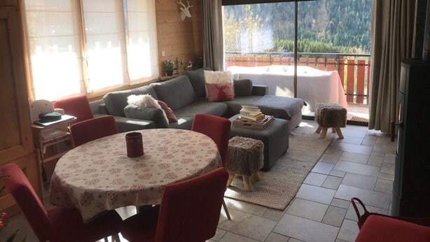 A cozy living room with a sofa, a dining table with chairs, and a view of a balcony with a table and chairs.