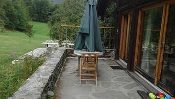 A stone patio with a wooden chair and table, a green umbrella, and colorful balls on a bench.