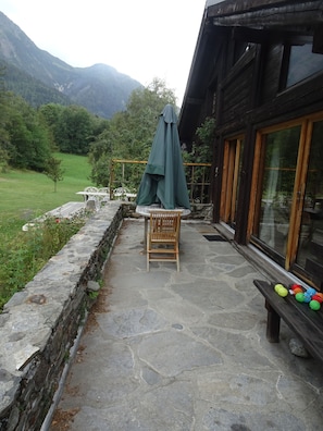 A stone patio with a wooden chair and table, a green umbrella, and colorful balls on a bench. - Renovated old farmhouse in Les Houches (Les Houches)