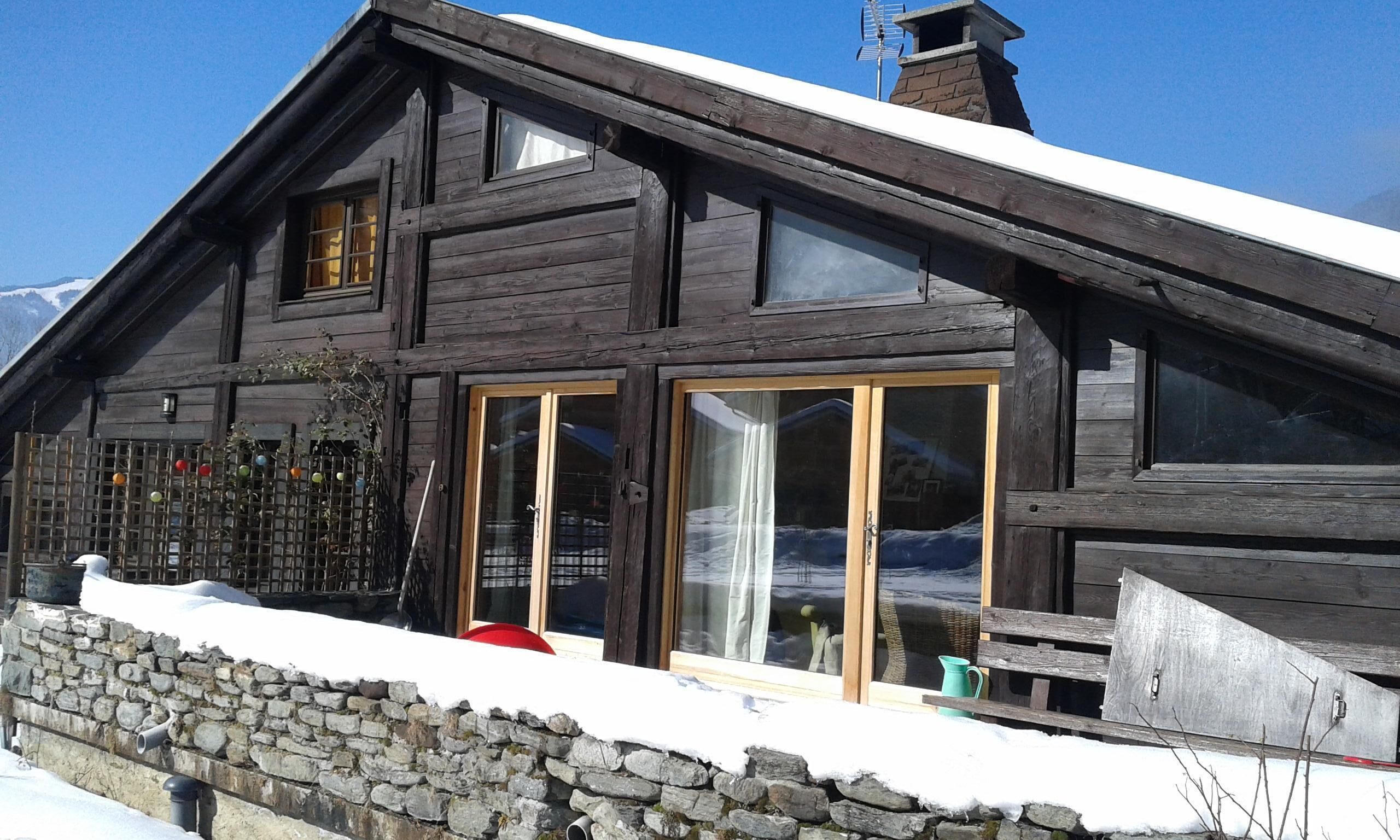 A wooden chalet with a stone foundation, large windows, and a chimney.