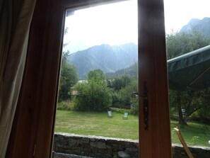 A view from a room with a wooden door, looking out to a grassy area with two chairs and a stone wall. - Renovated old farmhouse in Les Houches (Les Houches)