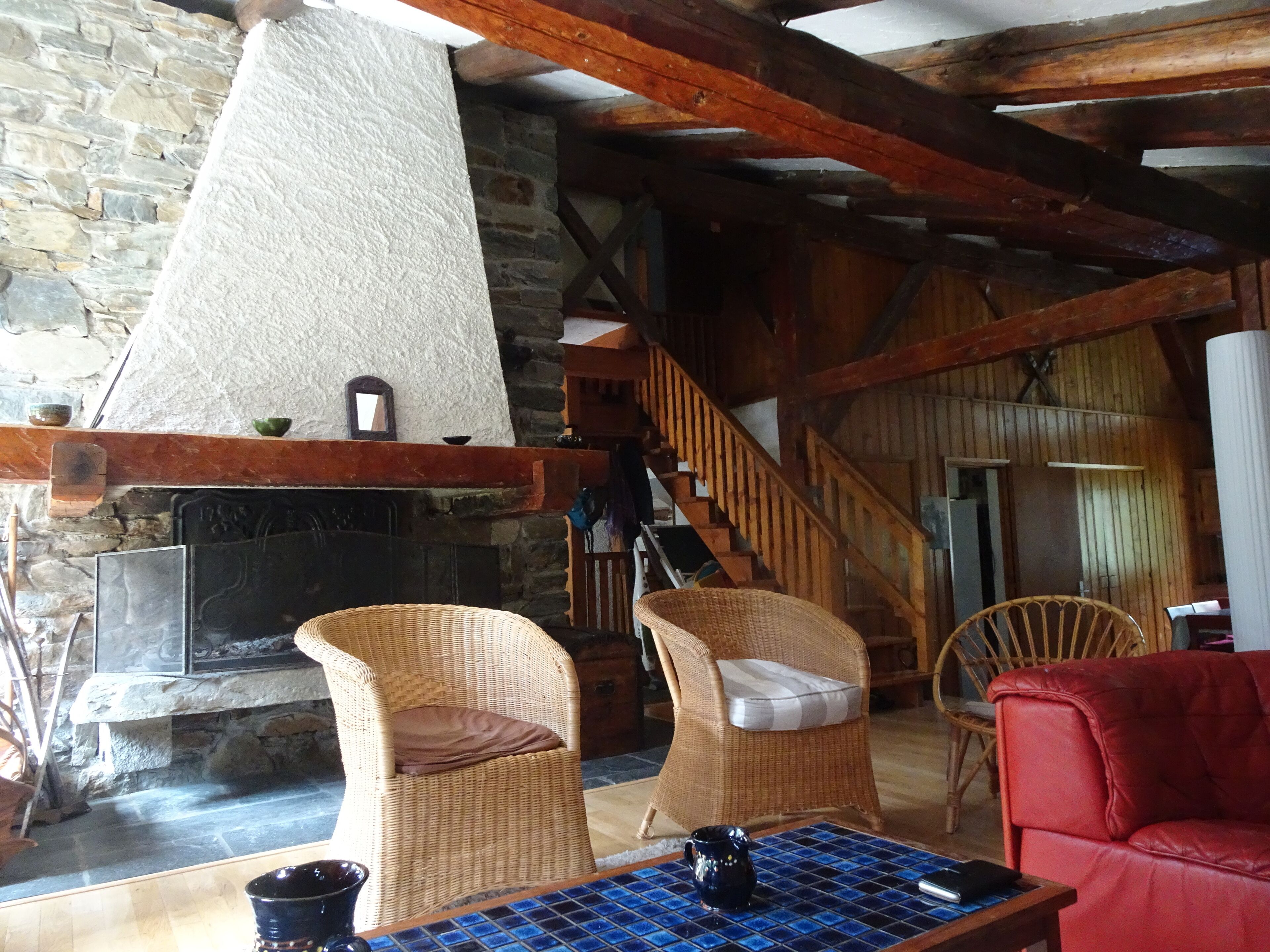 A rustic interior with a stone fireplace, wicker chairs, a red sofa, and a tiled coffee table.