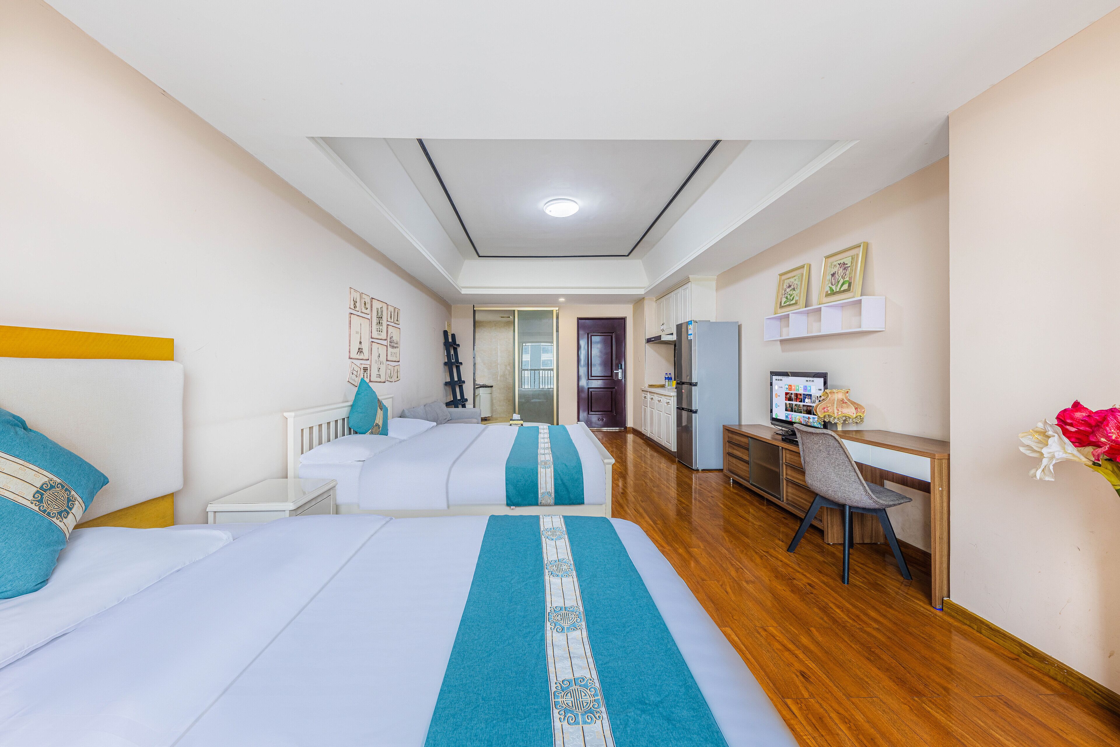Quarto de hotel com duas camas, uma escrivaninha, uma cadeira, um frigorífico e uma televisão.