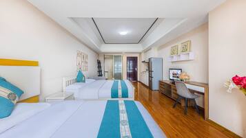 Quarto de hotel com duas camas, uma escrivaninha, uma cadeira, um frigorífico e uma televisão.
