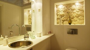A bathroom with a sink, mirror, toilet, and a stone wall feature. - Stylishly renovated stone villa w/fantastic sea view  (Lefkas)