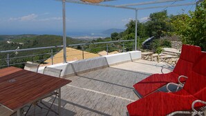 A covered outdoor seating area with a table and red chairs, overlooking a scenic landscape. - Stylishly renovated stone villa w/fantastic sea view  (Lefkas)