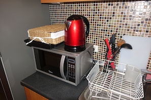 Compact kitchen area with microwave, kettle, and utensil rack.