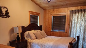 A cozy bedroom with a wooden ceiling, a bed with a quilted cover, a nightstand with a lamp, and a bookshelf. - WHISKEY SPRINGS CABINS #1
Cozy and delightful, in town convenience (West Yellowstone)