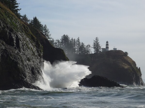 A lighthouse on a rocky cliff with waves crashing against it.