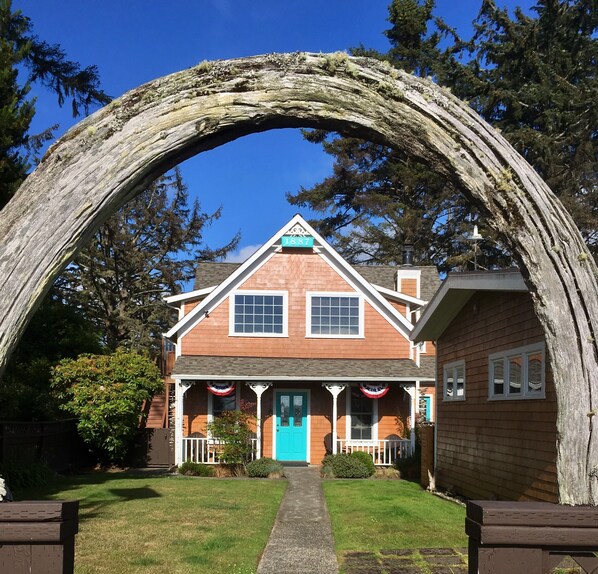 A house with a porch, a blue door, and a large tree arching over the entrance.