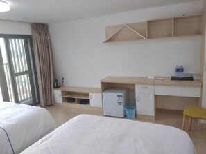 A hotel room with two beds, a desk, a small refrigerator, a water dispenser, and a trash bin.