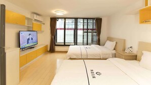 Ein Hotelzimmer mit zwei Betten, einem Fernsehgerät auf einem Schrank, einem Fenster mit Vorhängen und einer Deckenleuchte.