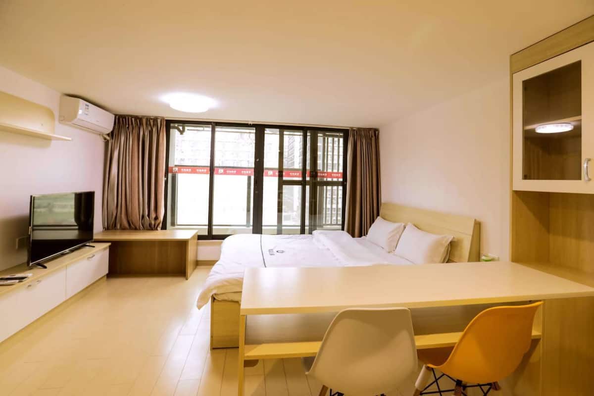 Una habitación de hotel con cama, escritorio, televisión y ventana con cortinas.