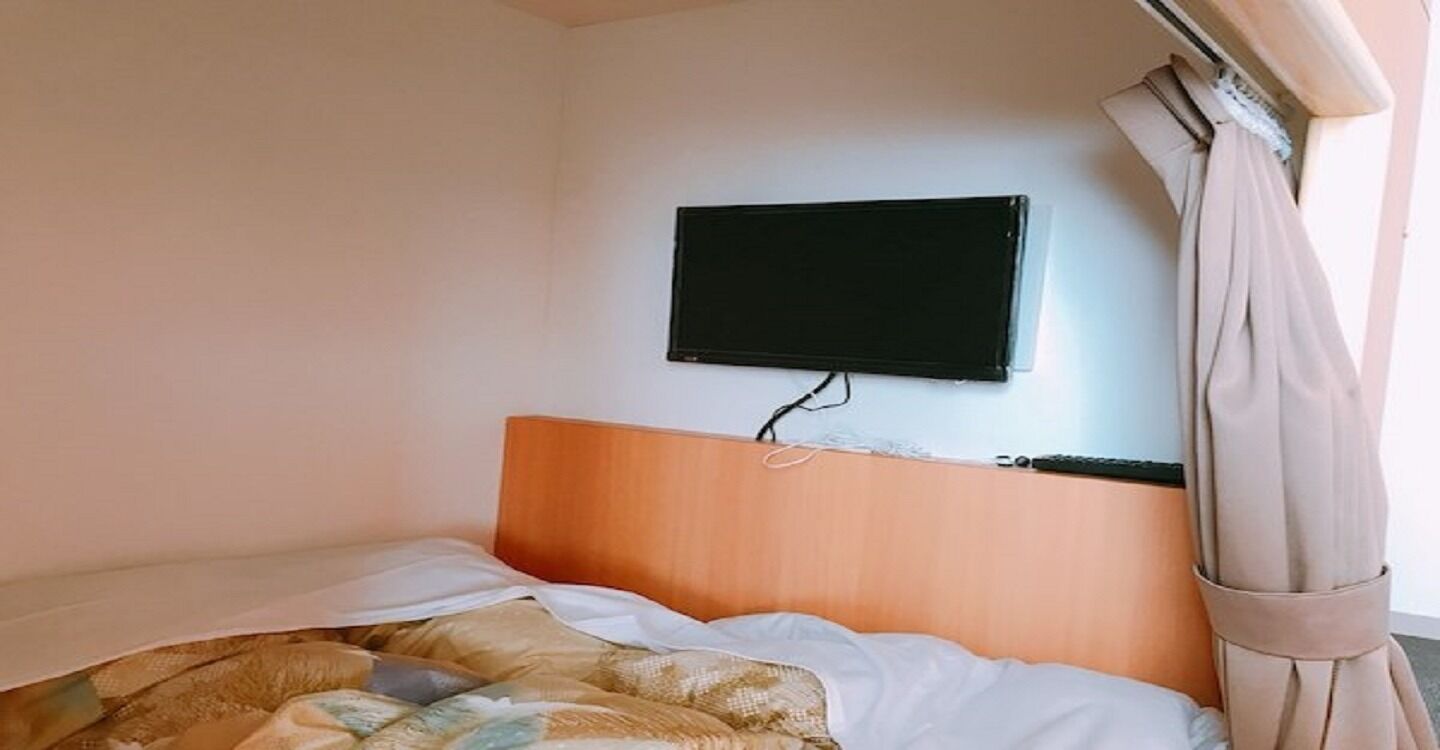 A hotel room with a bed, a television mounted on the wall, and a curtain.